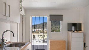 A modern kitchen with a sink, a wooden cabinet, a television on a stand, and a view of a mountainous landscape through a glass door. - Vacation Apartment 'Fewo Arafo' with Sea View, Private Terrace and Wi-Fi (Güímar)
