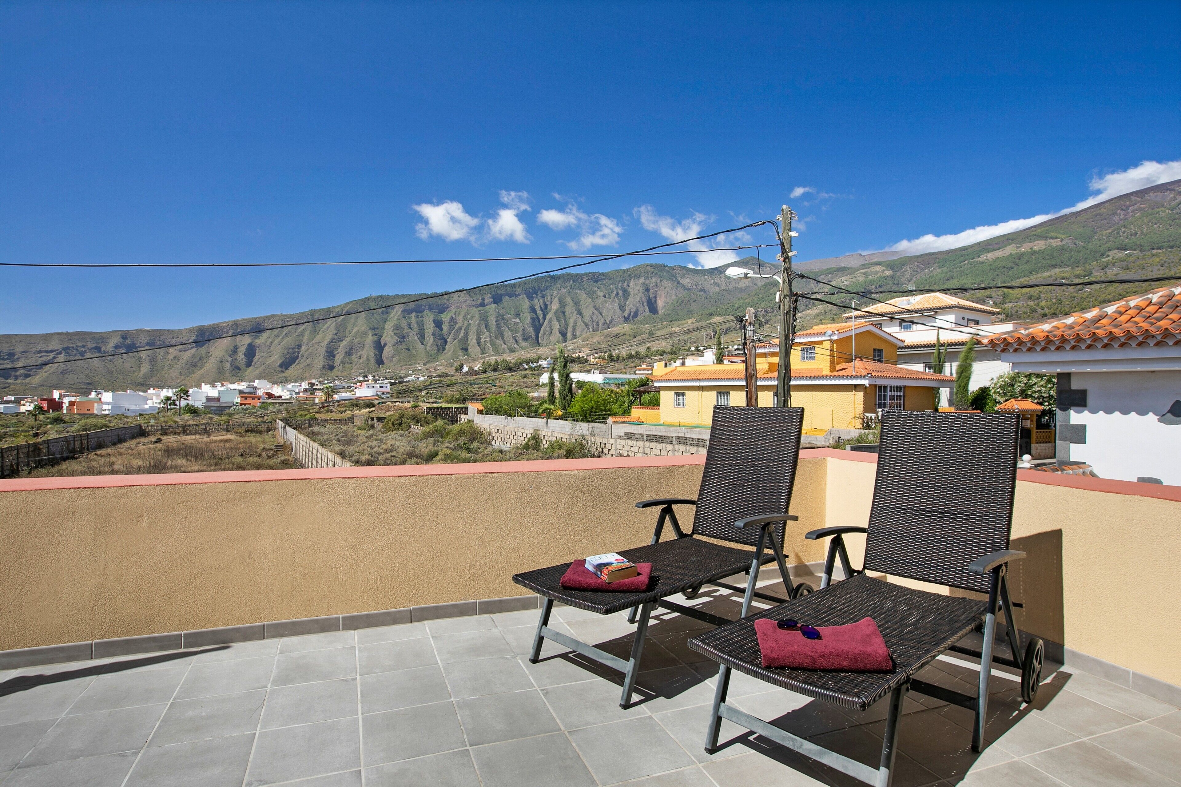 A balcony with two wicker chairs, a red cushion, and a book on one of the chairs.