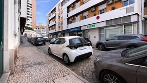 En gade med parkerede biler, en bygning med et 'DECO' skilt, og et 'CANTIO NOTARIAL' skilt.