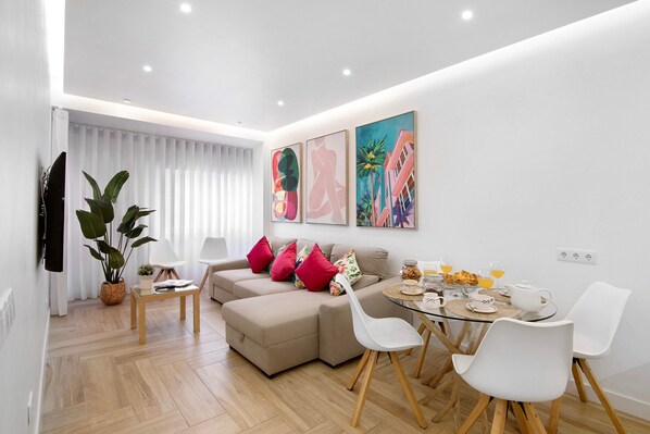 A modern living room with a sofa, dining table, chairs, and artwork on the wall.