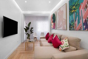 A modern living room with a flat-screen TV, beige sofa, red pillows, and abstract wall art.