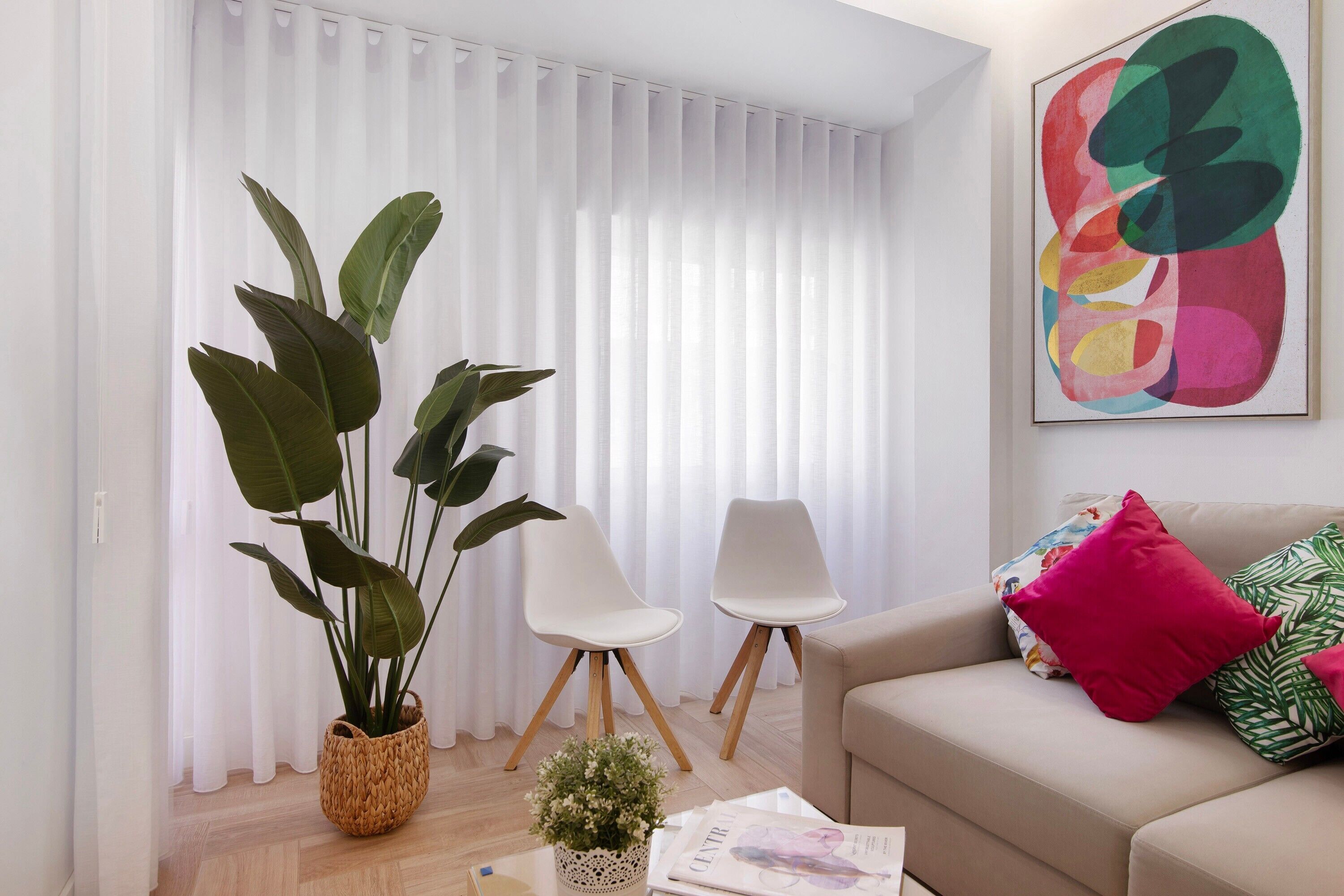 A living room with a sofa, two chairs, a potted plant, a coffee table, and a colorful abstract painting.