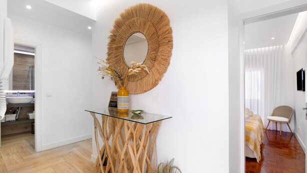 Ein modernes Interieur mit einem Glastische, einem gewebten Spiegel und einem Bett mit gestreifter Decke.