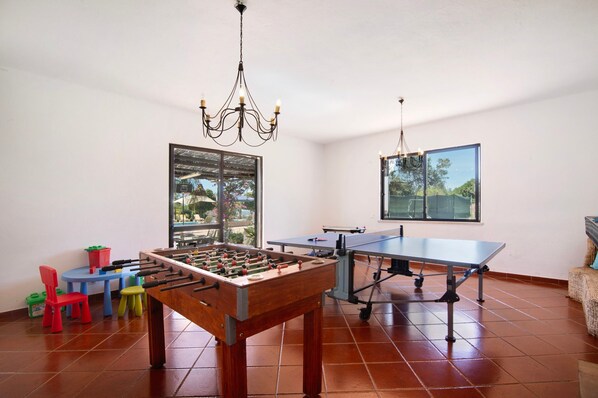 A room with a foosball table, a ping pong table, a chandelier, and a window with a view. - Country House 'Casa Da Avó' with Sea View, Wi-Fi and Air Conditioning (Loulé)