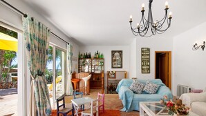 A living room with a sofa, a coffee table, a dining area with chairs, a chandelier, and a bookshelf. - Country House 'Quinta Da Ilda' with Sea View, Wi-Fi and Air Conditioning (Loulé)