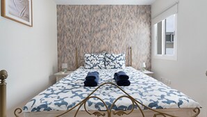Une chambre à coucher avec un lit, des oreillers, une table de chevet, une lampe et une fenêtre.
