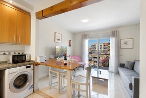 A compact kitchen with a washing machine, a microwave, and a dining area with a table and chairs.