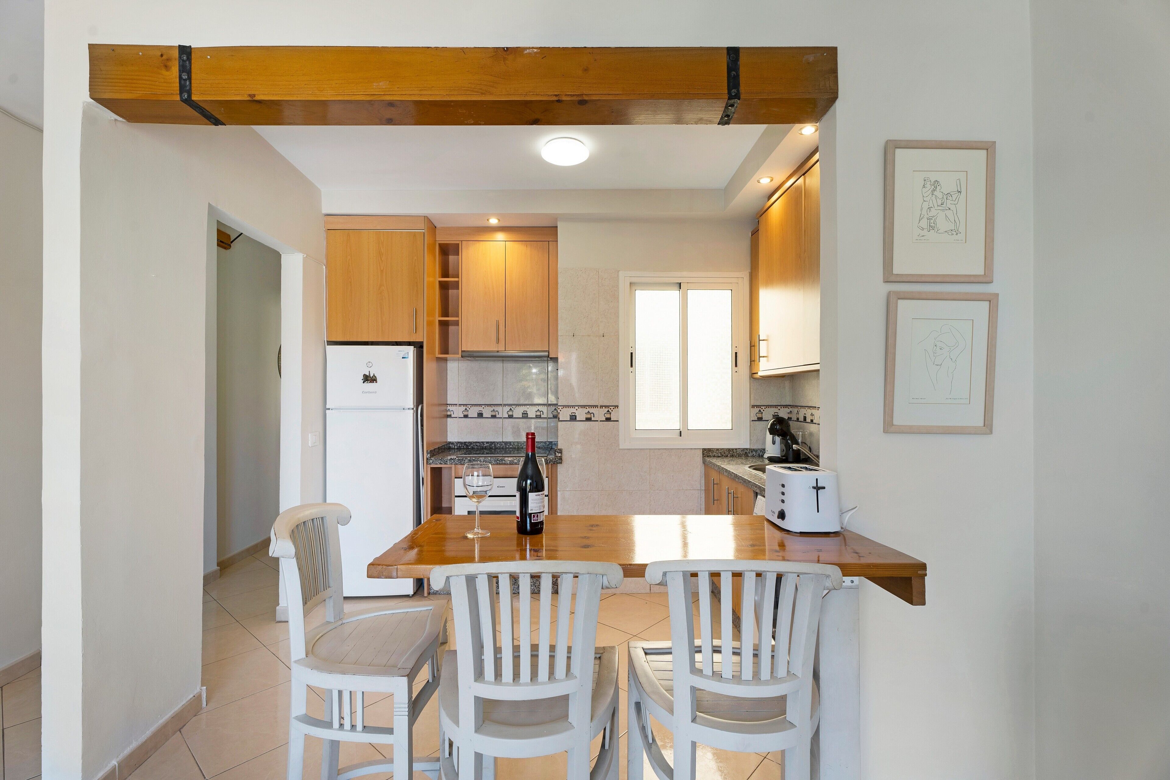 Una cocina con armarios de madera, un refrigerador blanco, una botella de vino y un tostador sobre la encimera.