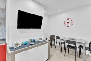 Une cuisine moderne équipée d’un téléviseur à écran plat, d’une horloge et d’un coin repas avec des chaises et une table.