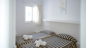 Habitació amb dos llits, una finestra amb cortines, un interruptor de llum fixat a la paret i un quadre amb marc.