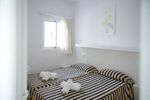 A room with two beds, a window with curtains, a wall-mounted light switch, and a framed picture. - Apartment 'Apartamento Ciel Azul' with Shared Pool, Balcony and Wi-Fi (Santa Eulalia del Río)