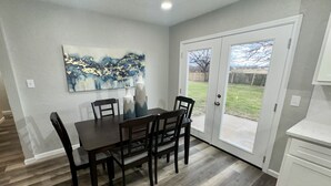 Un comedor con una mesa y sillas de madera oscura, un cuadro en la pared y un ventanal corredizo que da a un jardín.