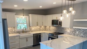 A modern kitchen with white cabinetry, a large island, a stainless steel stove, and pendant lighting. - Sunny, Beach Days - Enjoy the beach just steps away in Clinton, Connecticut  (Clinton)