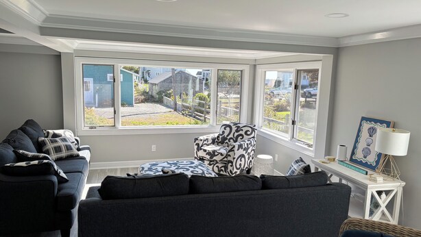 A living room with a dark grey sofa, a patterned armchair, and a white side table with a lamp and a framed picture. - Sunny, Beach Days - Enjoy the beach just steps away in Clinton, Connecticut  (Clinton)
