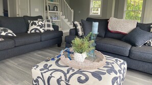 A modern living room with a grey sofa set, a coffee table with decorative items, and a staircase in the background. - Sunny, Beach Days - Enjoy the beach just steps away in Clinton, Connecticut  (Clinton)
