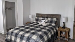 Un dormitorio con una cama grande, dos mesitas de noche con lámparas, un cabecero de madera y un armario con barra.