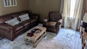 Una sala de estar con un sofá de cuero marrón, una mesa de centro de madera y un sillón de cuero.