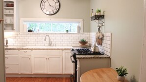 Una cocina con armarios blancos, encimera de granito, estufa y un reloj en la pared.