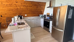 A modern kitchen with wooden walls, white cabinets, a stainless steel refrigerator, and a granite countertop. - Dock Holiday - beautiful views on Badin Lake.  Updated kitchen & game room (New London)