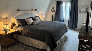 A bedroom with a large bed, a wooden nightstand with a lamp, a small table with a plant, and a window with curtains. - Dock Holiday - beautiful views on Badin Lake.  Updated kitchen & game room (New London)