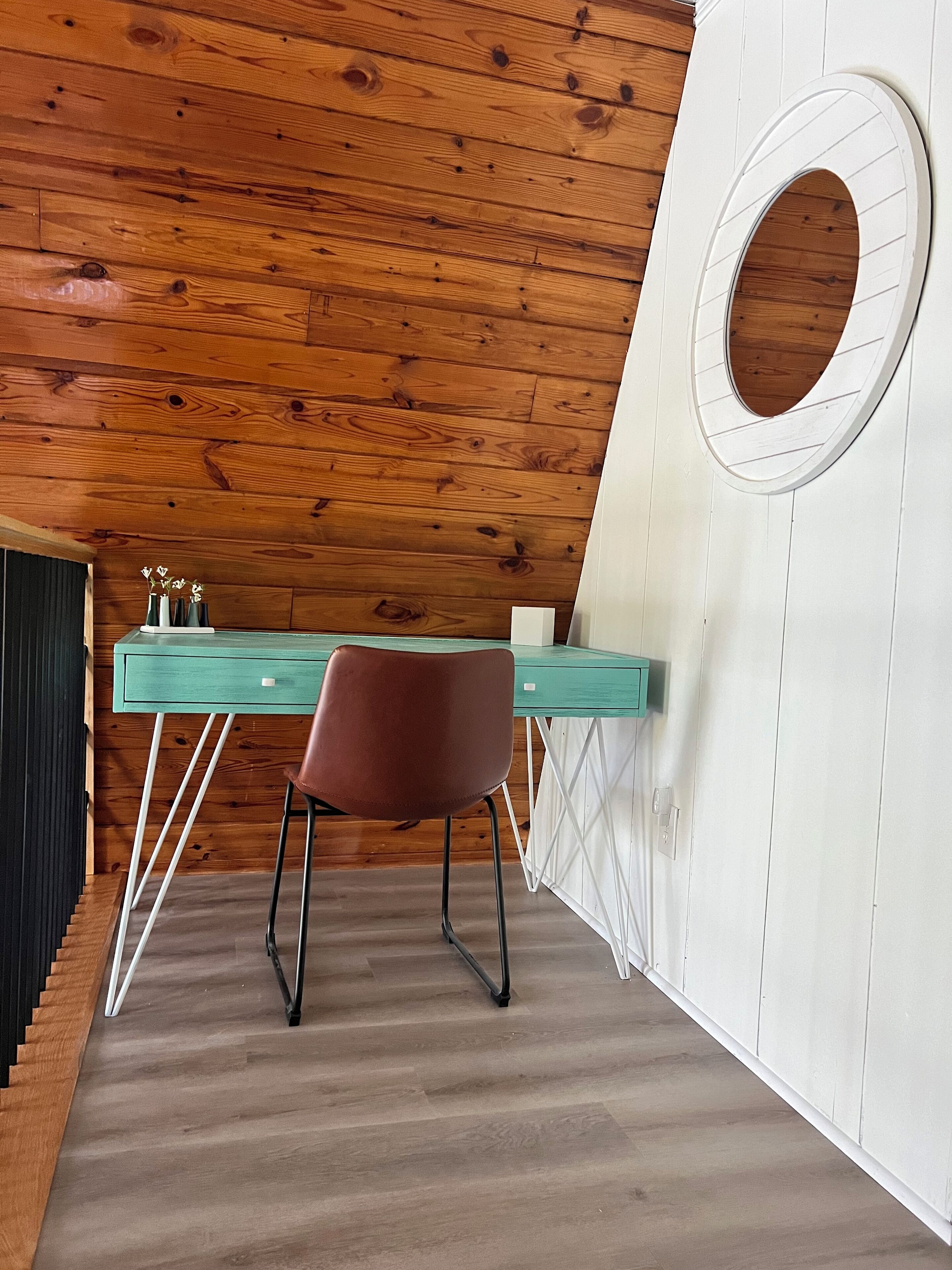 A room with a wooden ceiling, a desk with a chair, and a circular window.