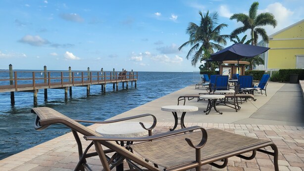 Eine Uferterrasse mit Liegestühlen und Tischen, ein hölzerner Steg, der ins Wasser führt, und im Hintergrund Palmen.