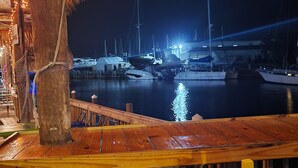 Ein Holzdeck mit einer Bank, mit Blick auf einen Yachthafen bei Nacht, wo Boote vor Anker liegen.