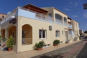 A two-story building with a balcony, potted plants, and a sign that reads "DASPINE STUDIOS". - Despina (Katerini)