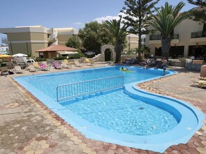 A swimming pool with a stone archway, lounge chairs, and palm trees.