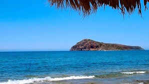 Une plage avec une île rocheuse à l’horizon et une structure à toit de chaume au premier plan.