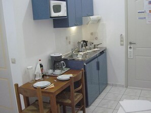 A compact kitchen with a microwave, coffee maker, and sink. There is a dining table with chairs and a small cabinet. - Despina (Katerini)