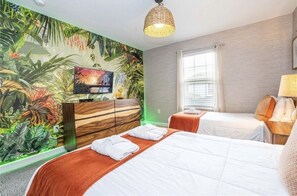A hotel room with a bed, a TV, a dresser, and a tropical mural on the wall.