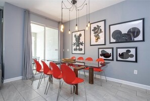 A dining area with a glass table, red chairs, and framed artwork on the wall.