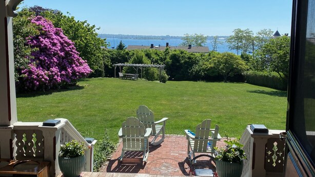 Un patio couvert avec des fauteuils Adirondack, une terrasse en bois et une vue sur une pelouse et un plan d’eau.
