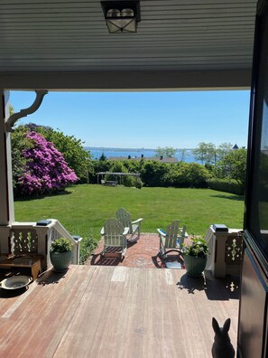Un patio techado con sillas Adirondack, una terraza de madera y vistas a un césped y un cuerpo de agua.