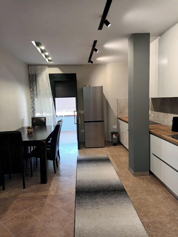 A modern kitchen with a refrigerator, a dining table with chairs, and a view to the outside. - Luander Hotel (Vaqarr)