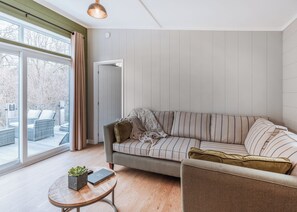 A modern living room with a sofa, a small round table with a plant, and a large window with curtains. - Willow Lodge VIP Hot Tub and Pet Friendly (Bridgnorth)