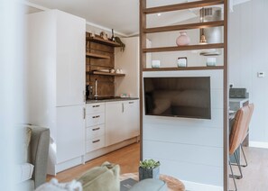 Una cocina moderna con armarios blancos, un televisor integrado y un estante de madera con objetos decorativos.