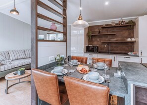 A modern dining area with a grey table, brown leather chairs, and a kitchen in the background. - Willow Lodge VIP Hot Tub and Pet Friendly (Bridgnorth)