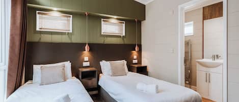 Habitación de hotel con dos camas, baño con lavamanos y una pared de acento verde.