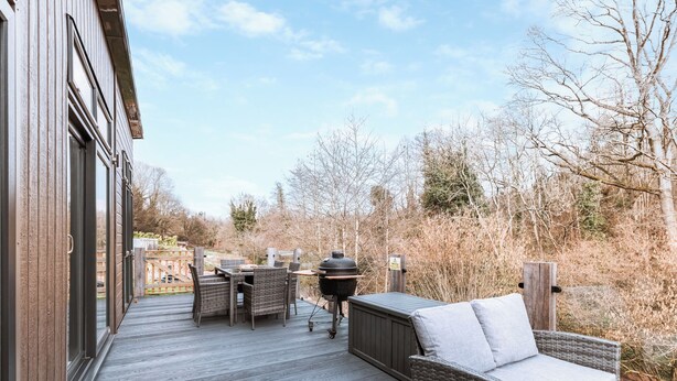 A wooden deck with wicker furniture, a barbecue grill, and a view of a wooded area. - Willow Lodge VIP Hot Tub and Pet Friendly (Bridgnorth)
