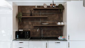 A modern kitchen with white cabinets, a black microwave, a sink, and decorative items on shelves. - Willow Lodge VIP Hot Tub and Pet Friendly (Bridgnorth)