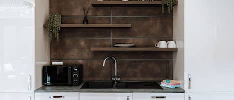 A modern kitchen with white cabinets, a black microwave, a sink, and decorative items on shelves.