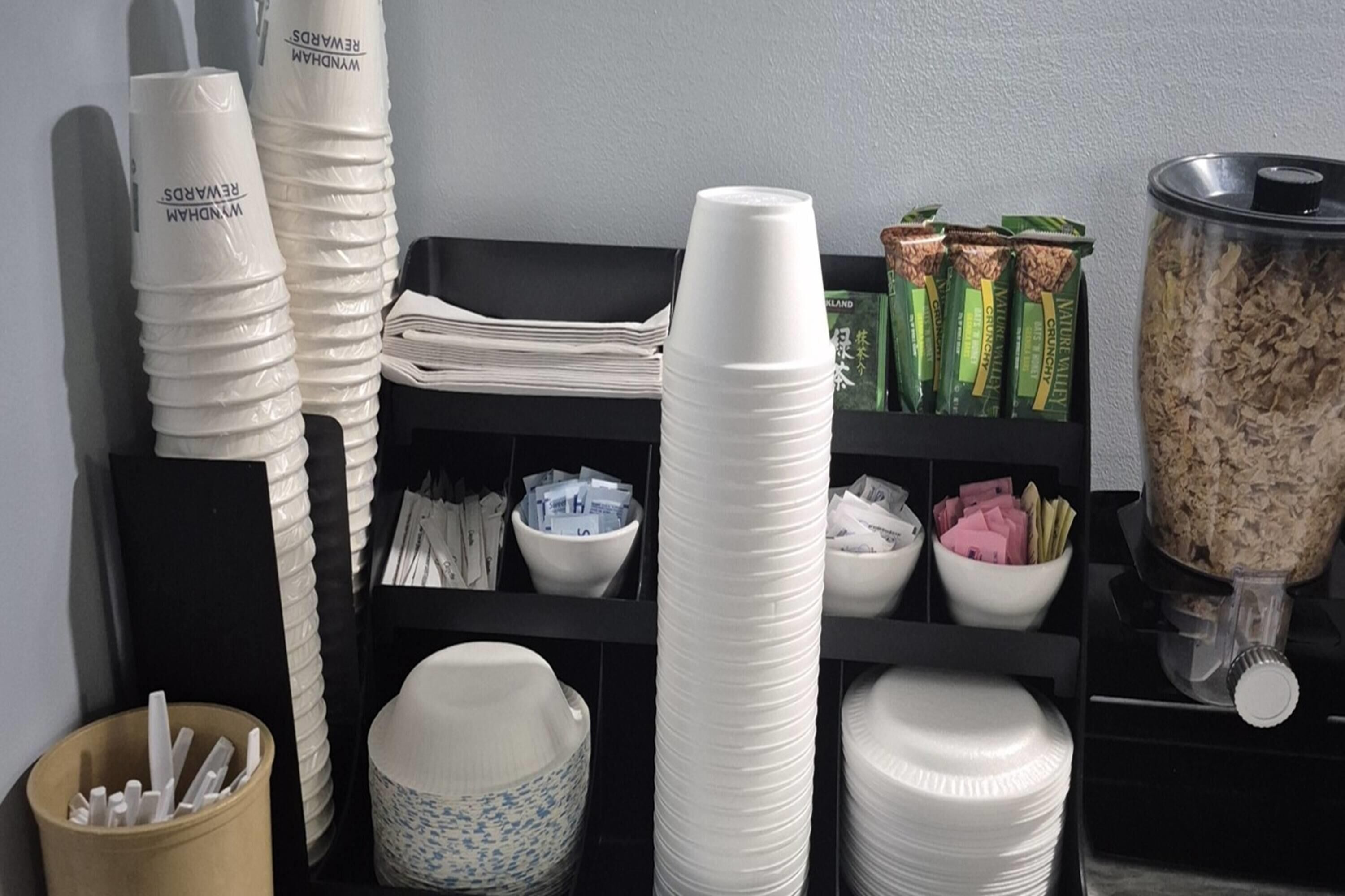 Pilha de copos de papel brancos, uma tigela com padrão azul e branco e um recipiente com itens verdes e castanhos.