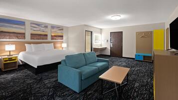 Ein Hotelzimmer mit Bett, Sofa, Schreibtisch, Fernseher, Spiegel und Kunstwerken an der Wand.