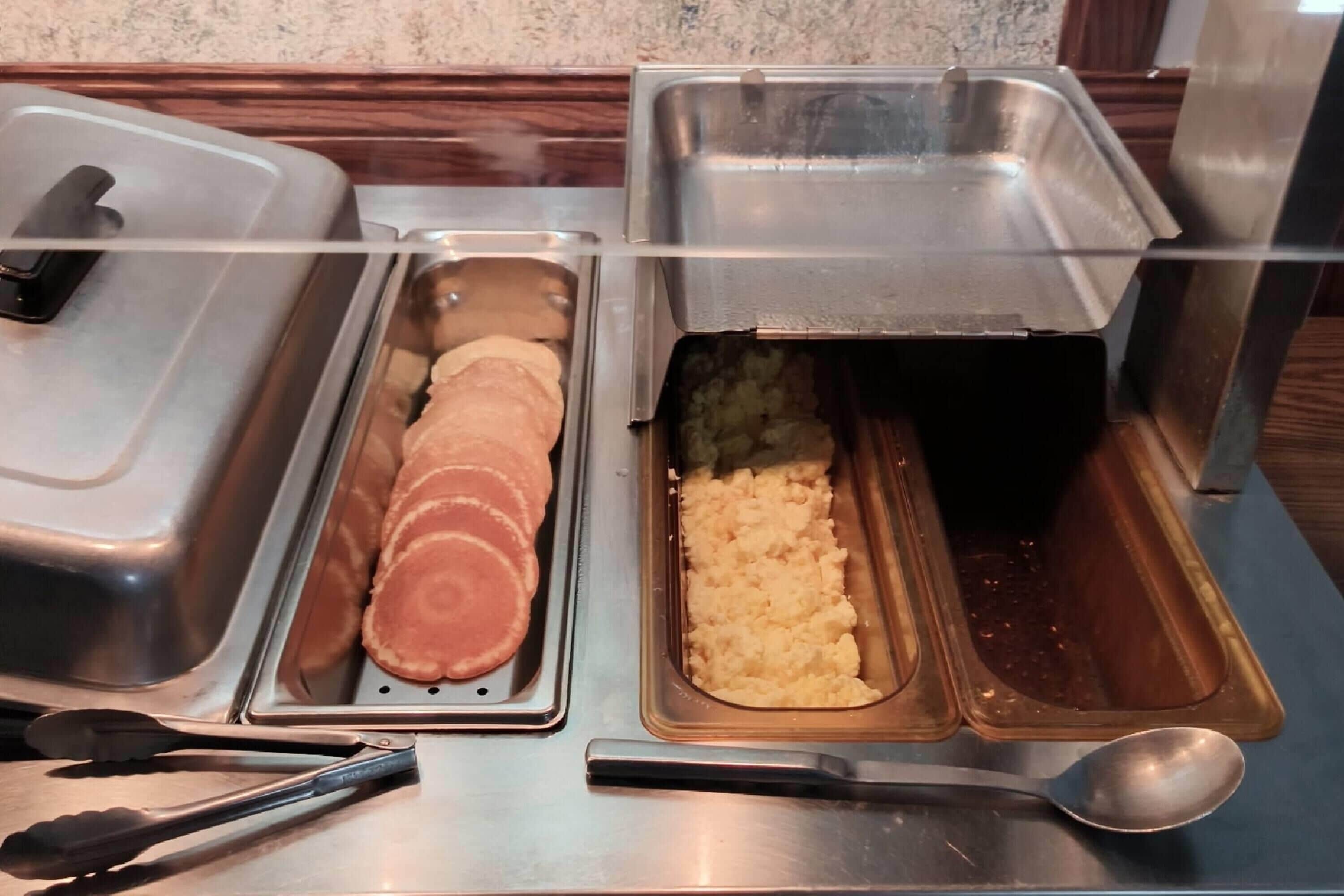 A buffet setup with various food items in metal containers, including sliced meat and mashed potatoes.