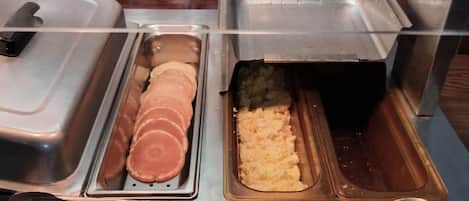 A buffet setup with various food items in metal containers, including sliced meat and mashed potatoes.