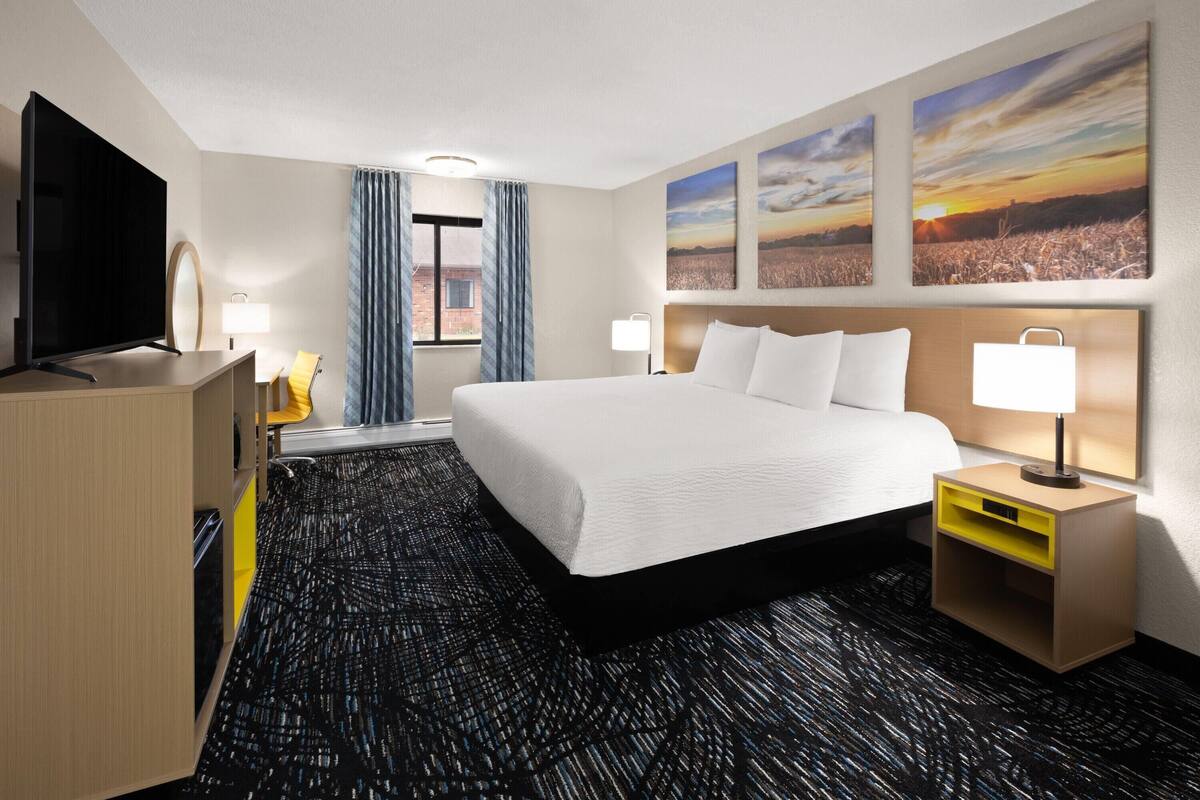 A hotel room with a large bed, a TV, a desk, and a window with curtains.