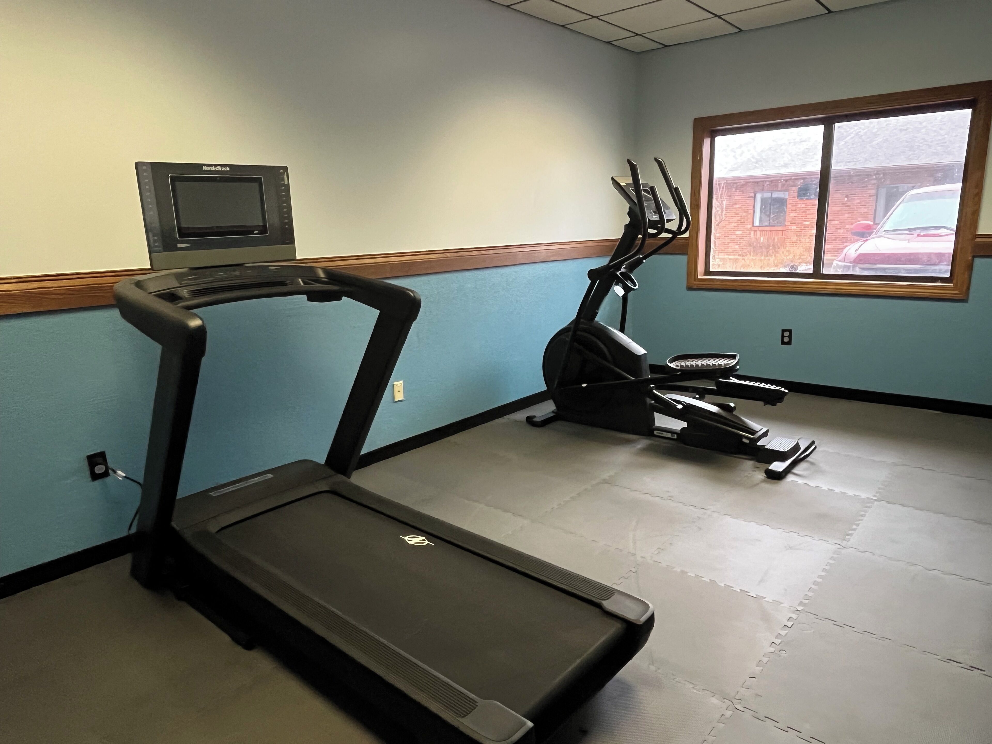 A fitness room with a treadmill, an elliptical, and a wall-mounted heart rate monitor.