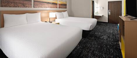 A hotel room with two beds, a desk, a TV, and artwork on the wall.